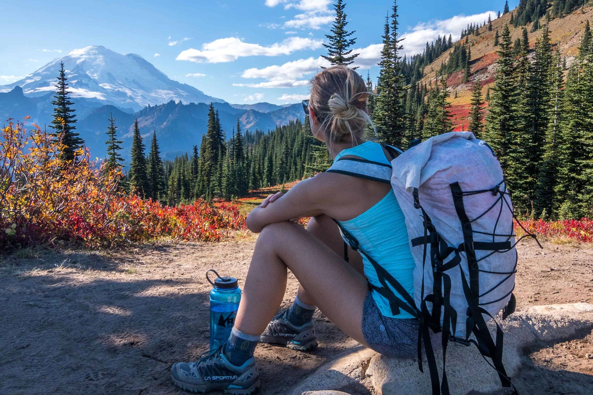 A woman with a backpack sitting on a rock overlooking a mountain.