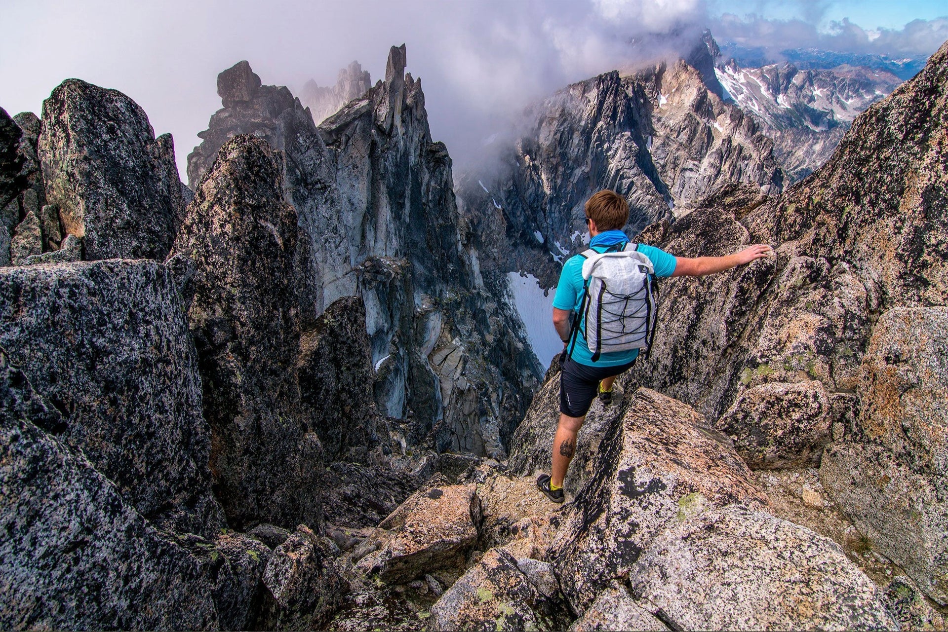 A man standing on top of a mountain with clouds in the background.